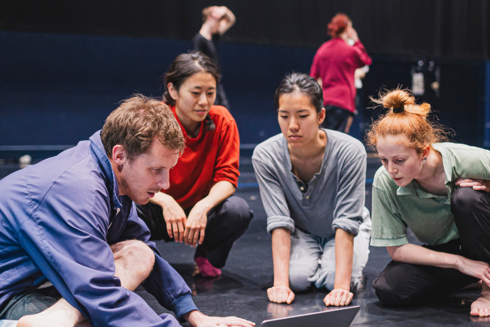 People collaborating sat around a laptop in a rehearsal space
